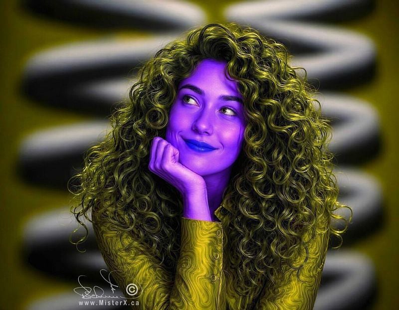 This digital artwork features a stylized portrait of a smiling woman with vibrant purple skin and a thick mane of voluminous, olive-green curly hair. She rests her chin on her hand in a contemplative or daydreaming pose, looking off to the side with bold, dark blue lipstick that contrasts against her purple complexion. She wears a long-sleeved silk blouse featuring intricate swirling olive-green patterns that blend smoothly into her hair color. The background is softly blurred, showing a repeating, abstract pattern of curved black and off-white shapes under a moody, directional light that highlights the detailed textures of her curls and clothing.