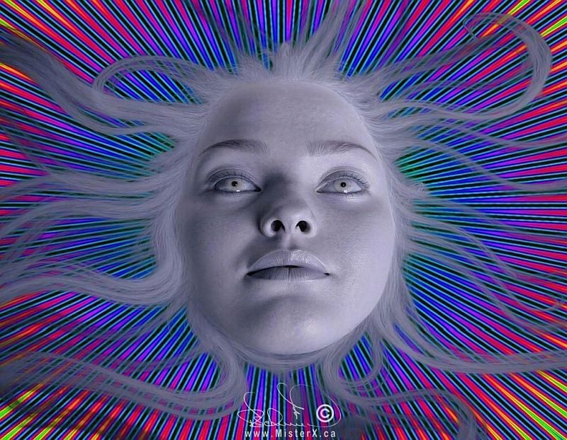 This psychedelic digital artwork features a pale, ghostly woman's face looking directly upward, her pale eyes wide and her long, silvery-white hair floating outward like wispy tendrils in all directions. Her monochromatic, nearly translucent skin contrasts sharply with the background, which consists of a vibrant, repeating radial sunburst pattern radiating outward from her face. This geometric background is composed of countless fine, multi-colored lines in electric shades of pink, blue, yellow, and green set against black intervals, creating a dizzying, hypnotic optical illusion that frames her head like a celestial halo.