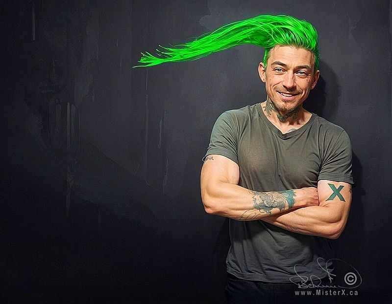 A smiling man in a tee-shirt is seen looking at the viewer. He has various tattoos and a huge improbable green hairdo. Set against a dark background.